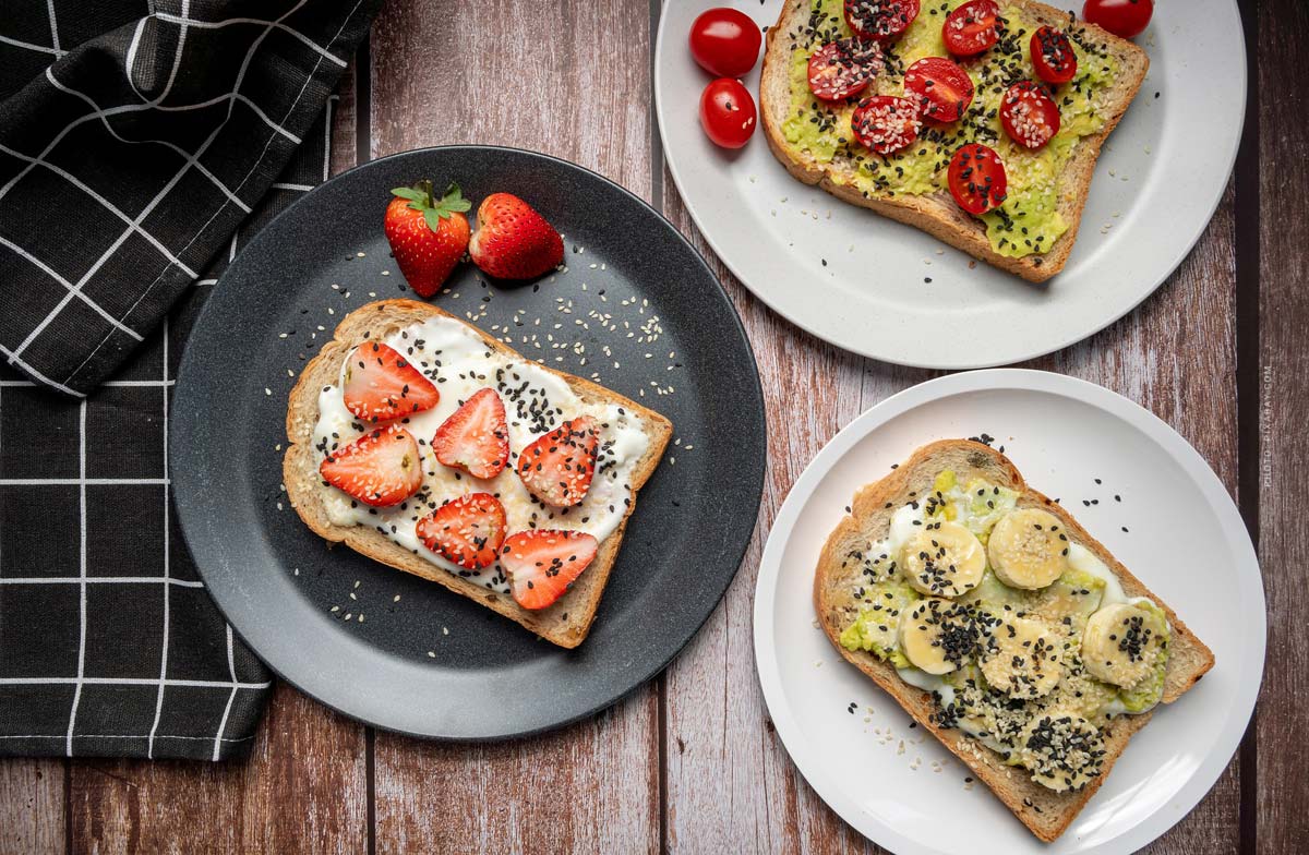 brot-avocado-erdbeere-banane-frischkaese-teller-schwarz-weiss-tischplatte