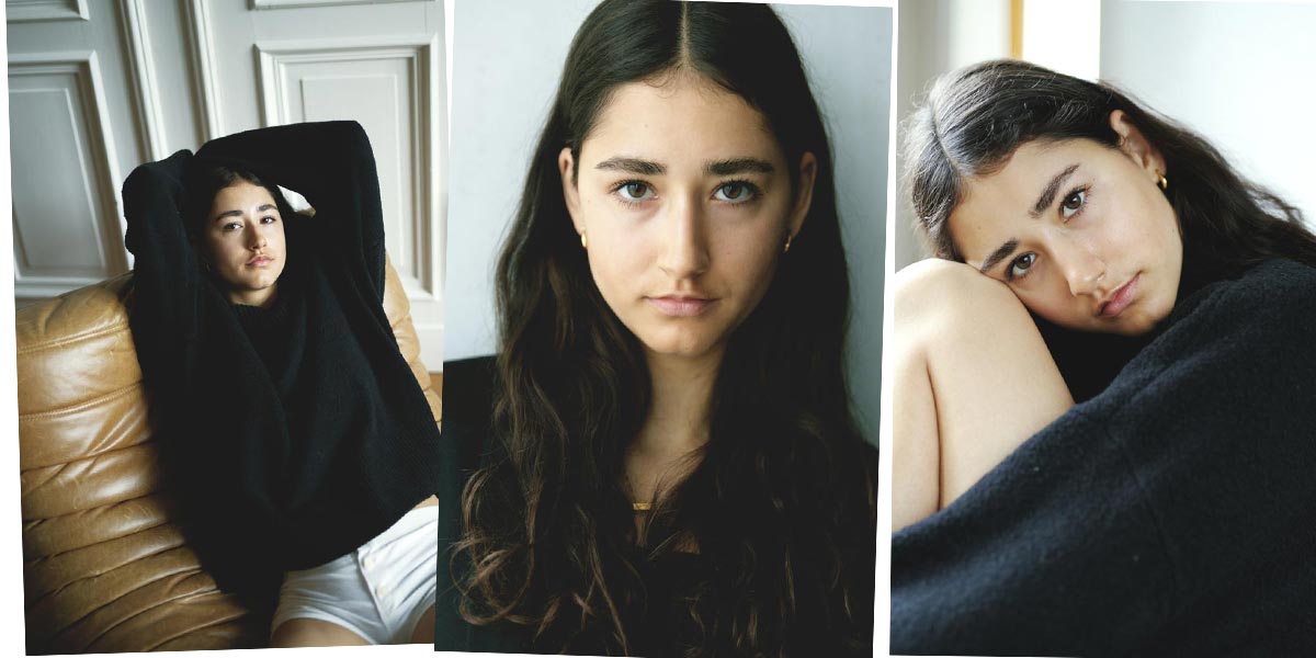 thumbnail–female-model-brown-curly-hair-berlin-white-pants-black-shirt-living-room-sitting-brown-couch